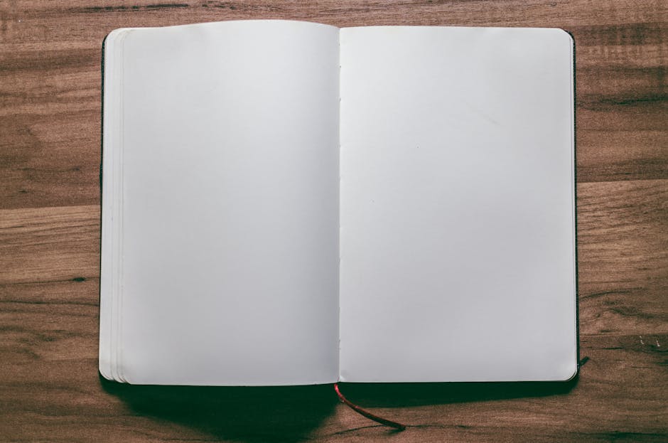 A top-down view of an open blank notebook on a wooden desk, perfect for design or writing projects.