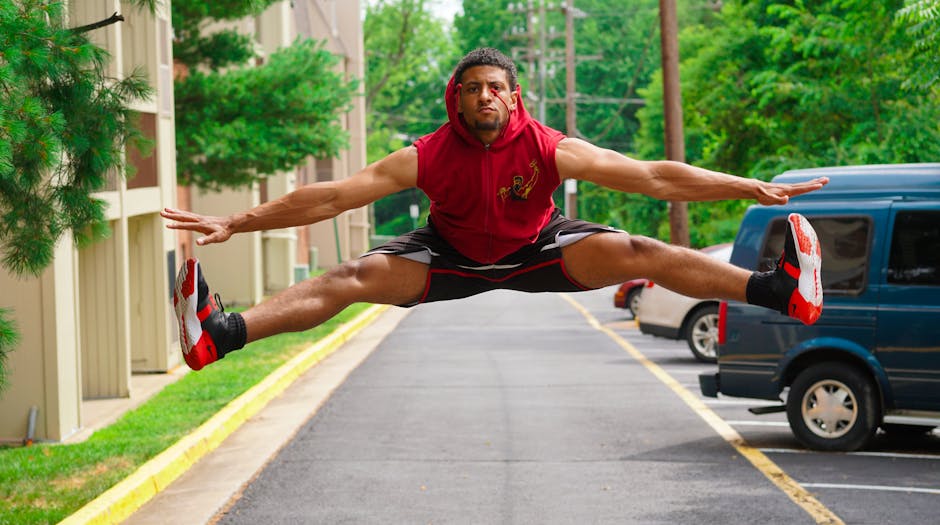 A young man in athletic wear performing a high jump outdoors in a parking area, showcasing fitness and agility.