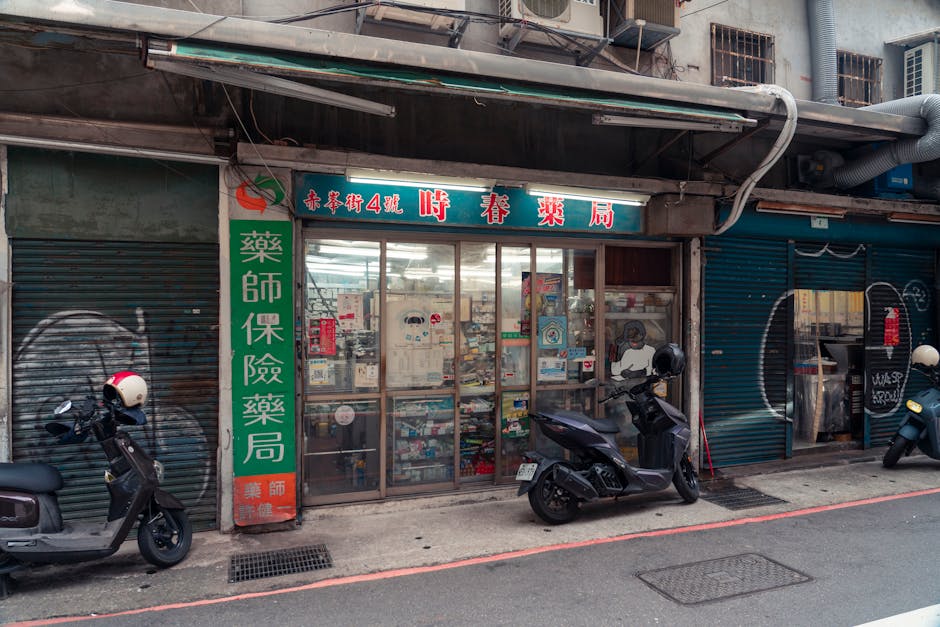 A bustling city street features scooters parked by an urban storefront.