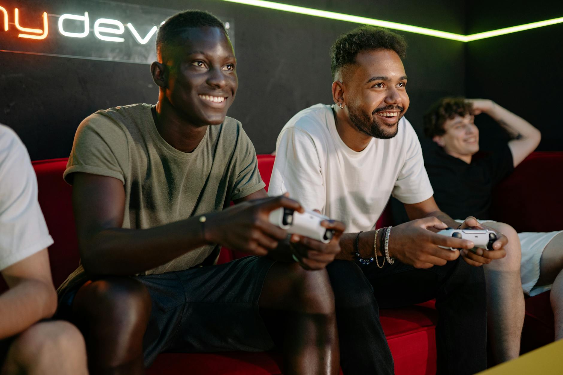 A group of friends energetically playing video games on a couch, smiling and engaged.