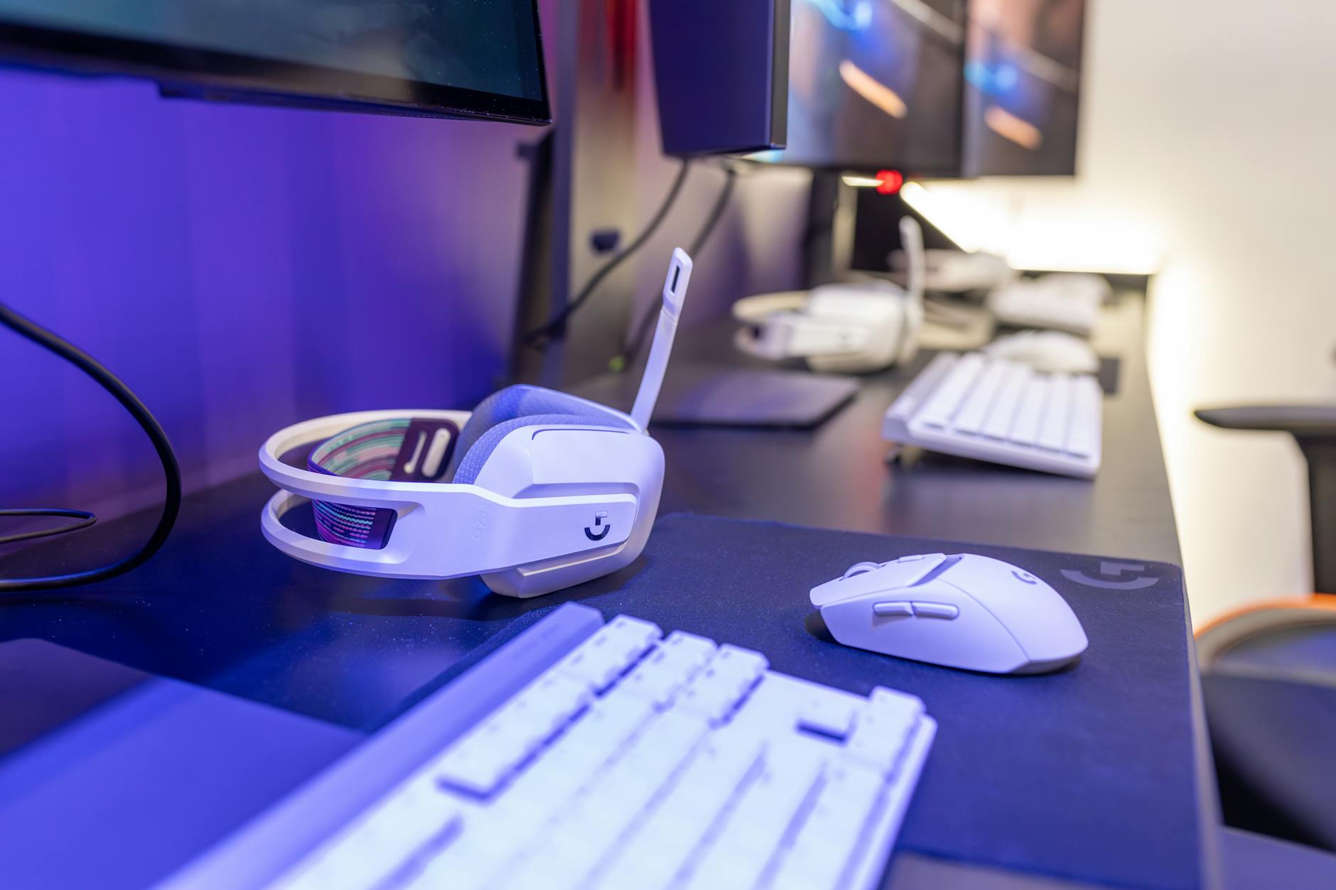 Close-up of a gaming setup featuring a white headset, computer mouse, and keyboard with a vivid lighting ambiance. – buying mice and peripherals