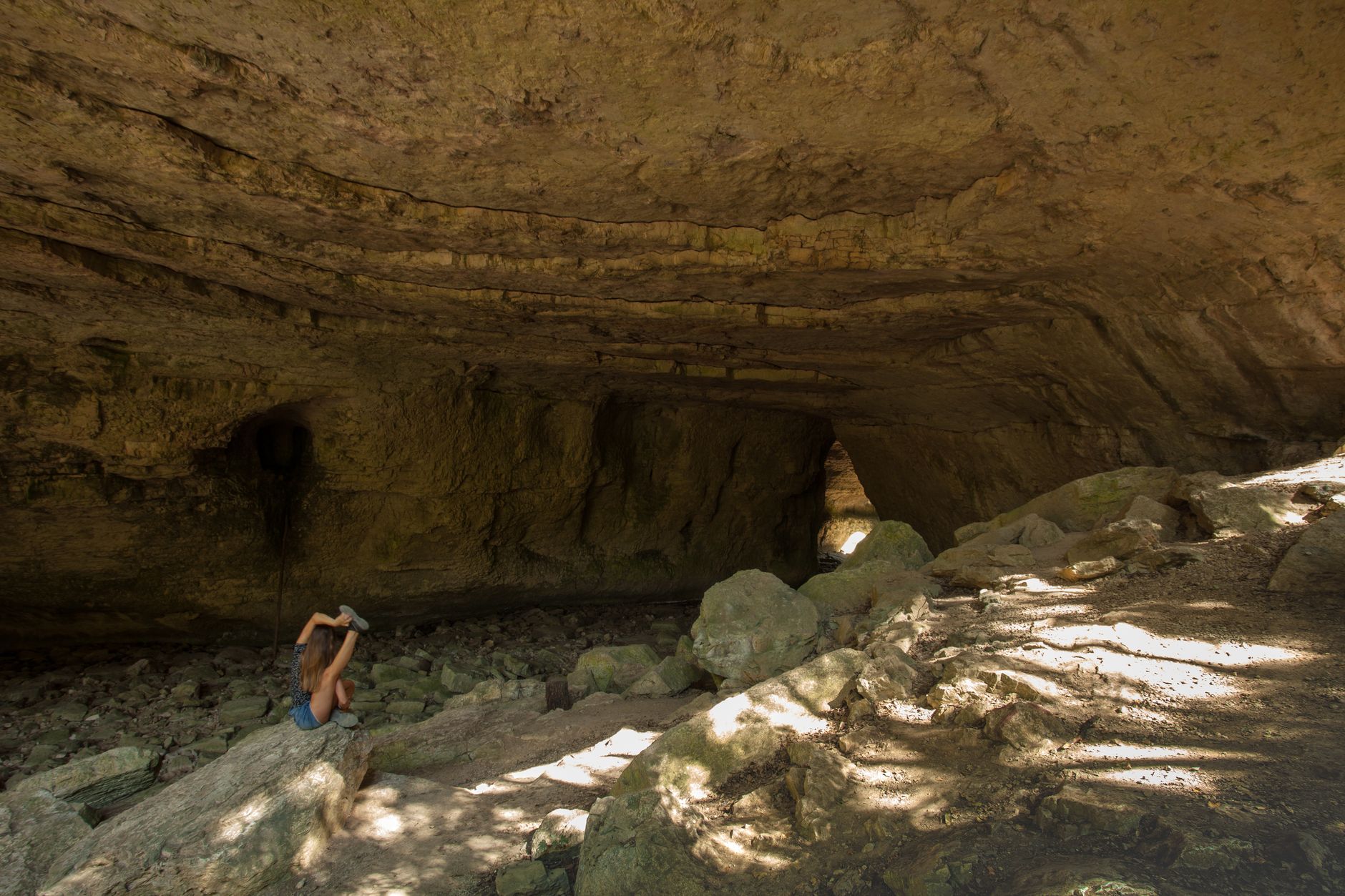 Adventurous scene of a person exploring a stone cavern under natural daylight.