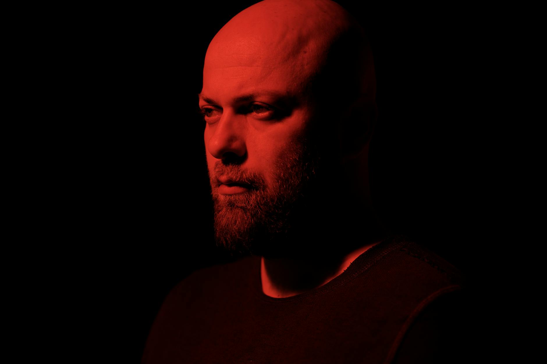 A bald man with an introspective expression under dramatic red lighting.