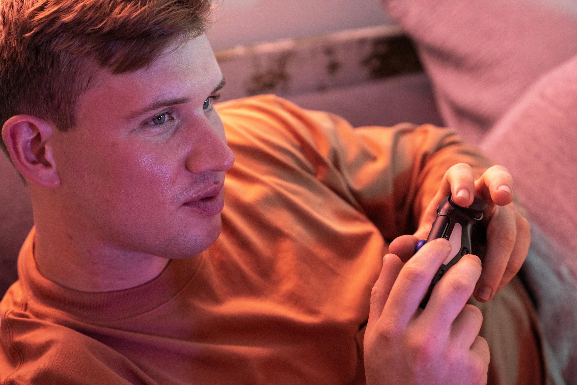 A young man plays video games on a comfortable couch, fully immersed in the experience.