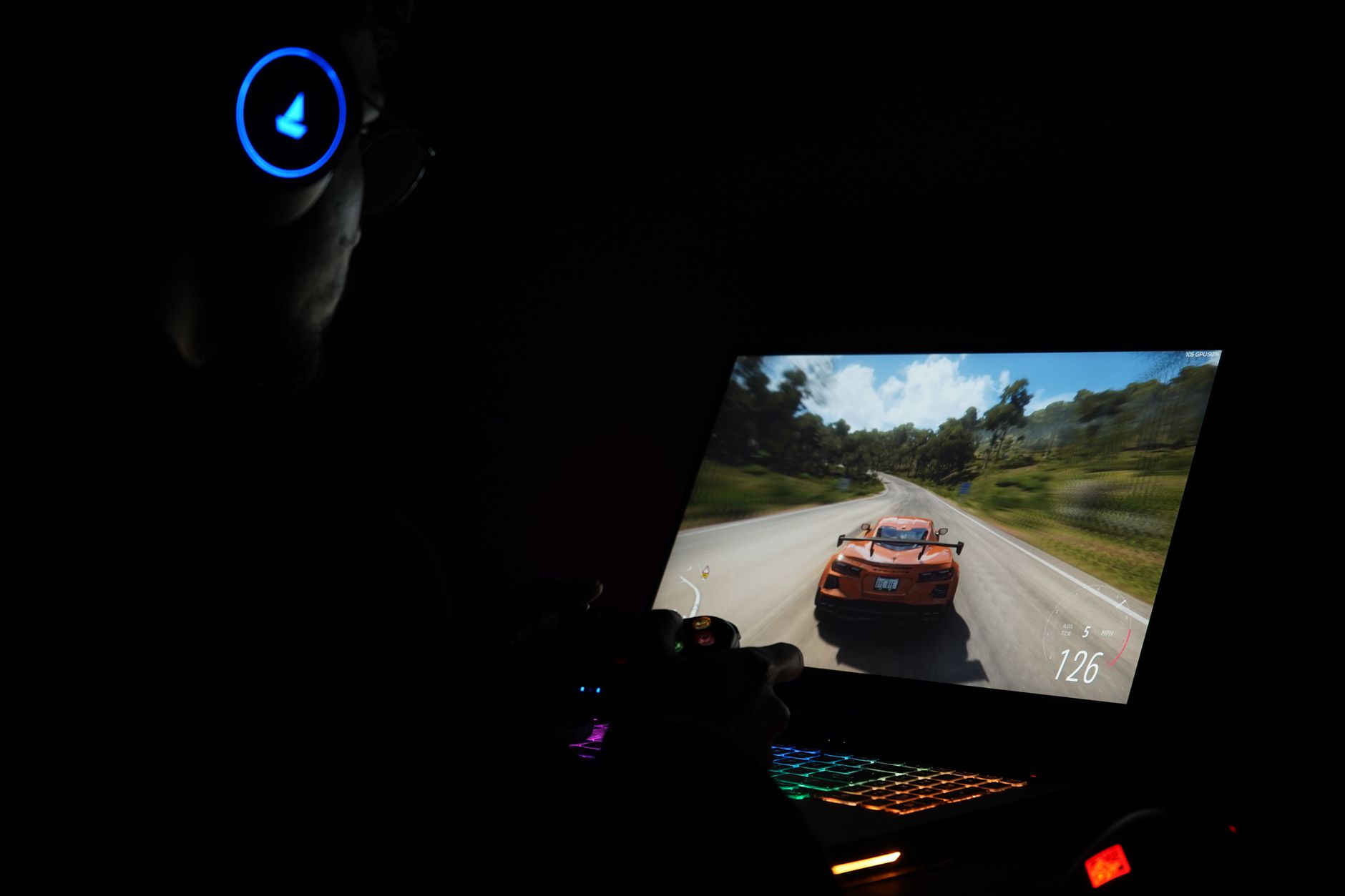 A gamer using a laptop and headphones to play a car racing game in a dark setting. – Forza Horizon 6 best settings