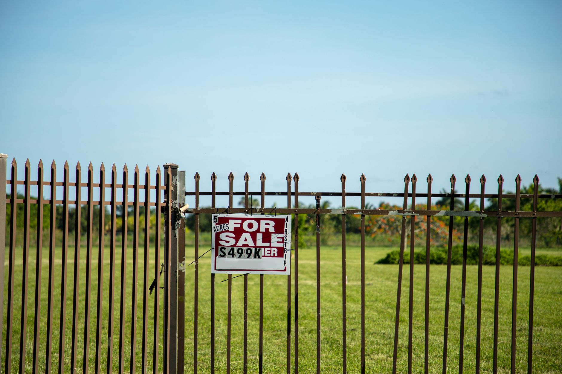 A large plot of land bordered by an iron fence, complete with a 'For Sale' sign in Miami, FL. Ideal for development. – Frontier Developments Sale 2026