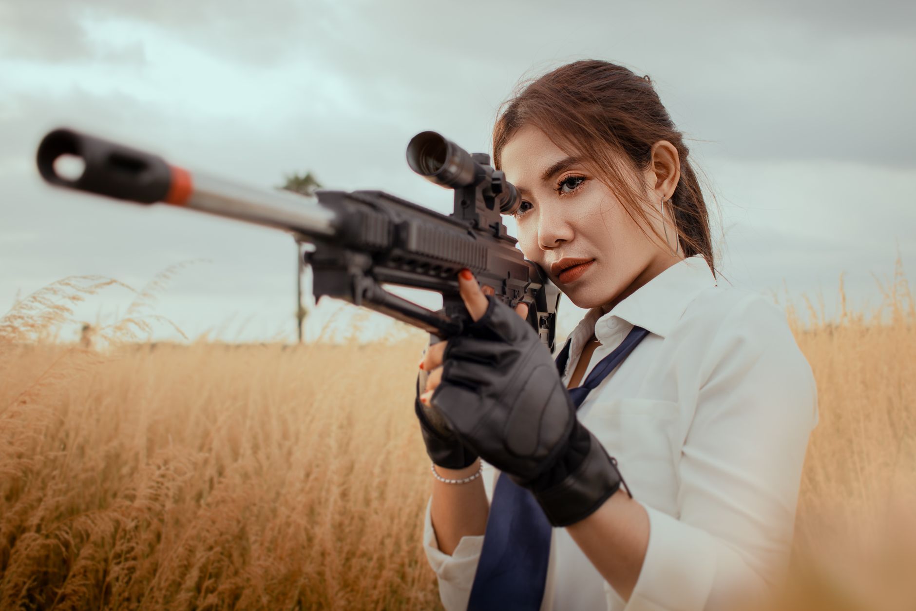 Stylish young Asian female taking aim with rifle while practicing in shooting on grassy field on cloudy day – shooting fps open world