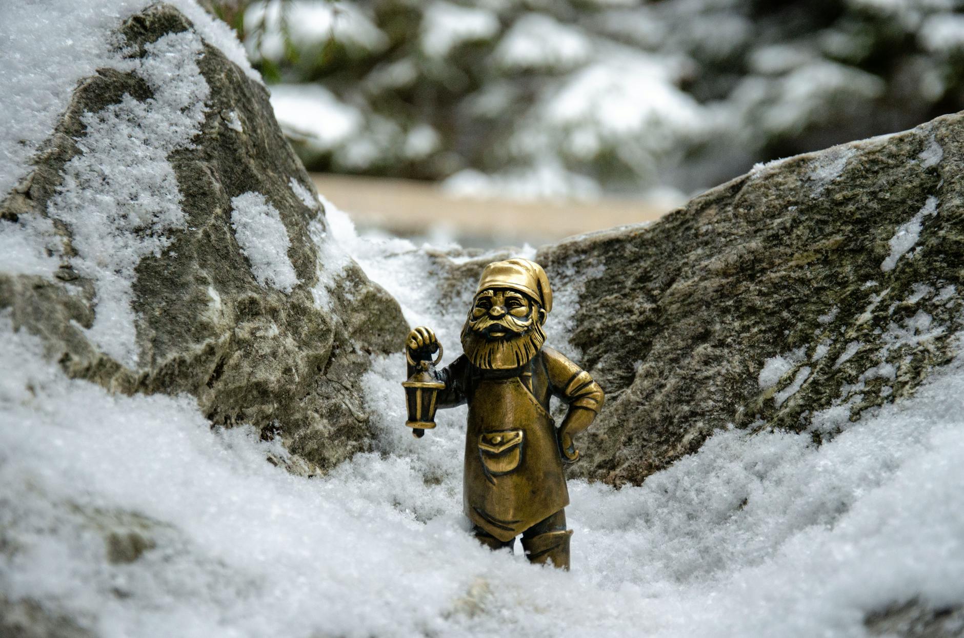A bronze gnome figurine holding a lantern, nestled among snow-covered rocks. – outbound gnomes