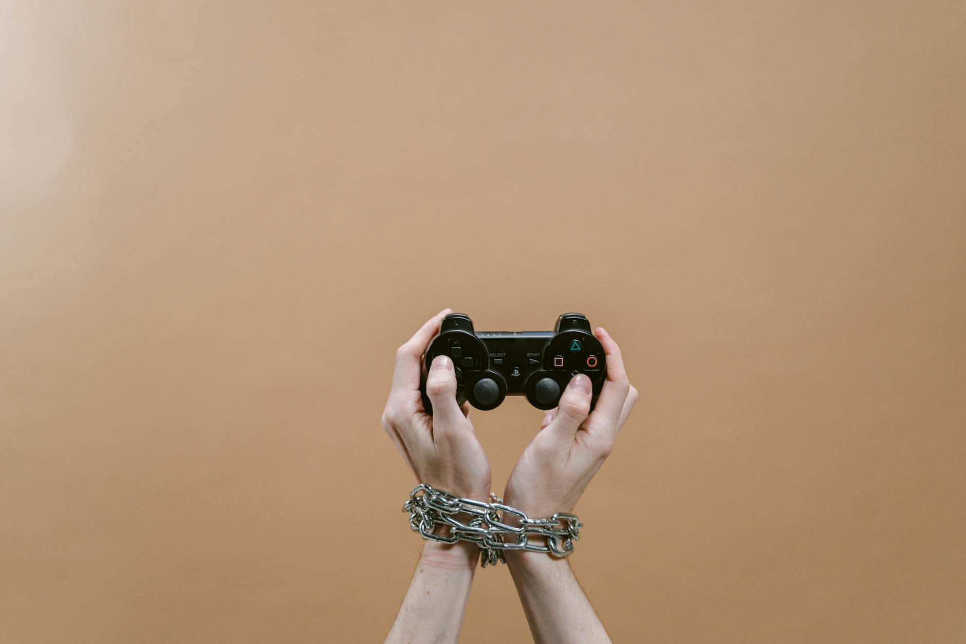 Conceptual image of hands in chains holding a game controller symbolizing gaming addiction.