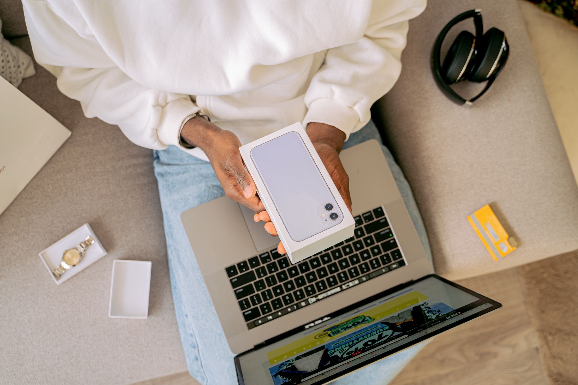 Person unboxing a new smartphone while sitting with a laptop, ready for online shopping on a cozy sofa.