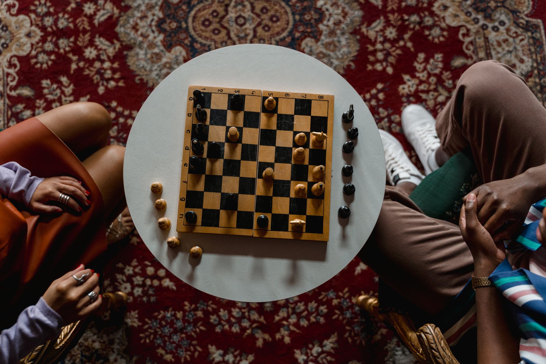 Overhead view of a chess game between two people seated indoors, focused on strategy.