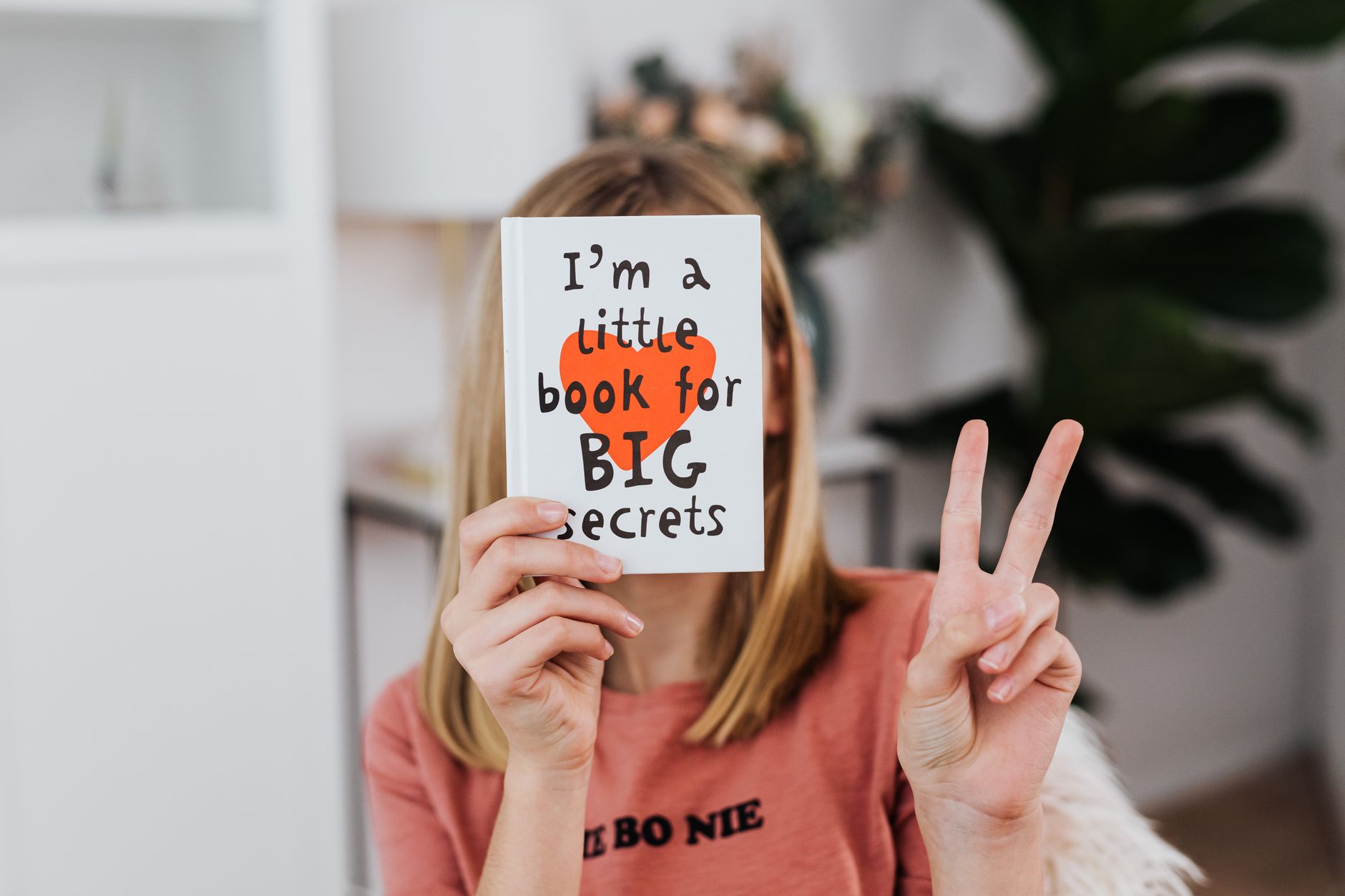 A woman holding a book with text and making a peace sign, conveying a playful and secretive mood. – aniimo secrets