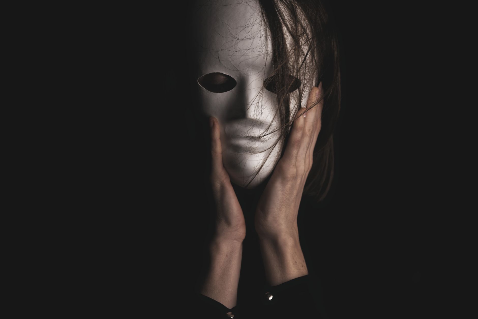 An eerie, dramatic portrayal of a person clutching a white mask, enveloped in darkness.